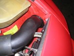 The pipe exits the engine bay through the stock air intake hole after passing over the headlight stop adjustment arm and linkage.